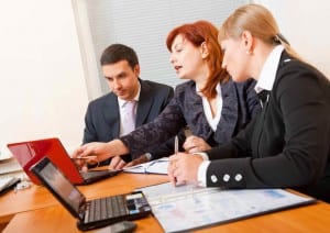 Two women and a man discuss what is on the man's laptop